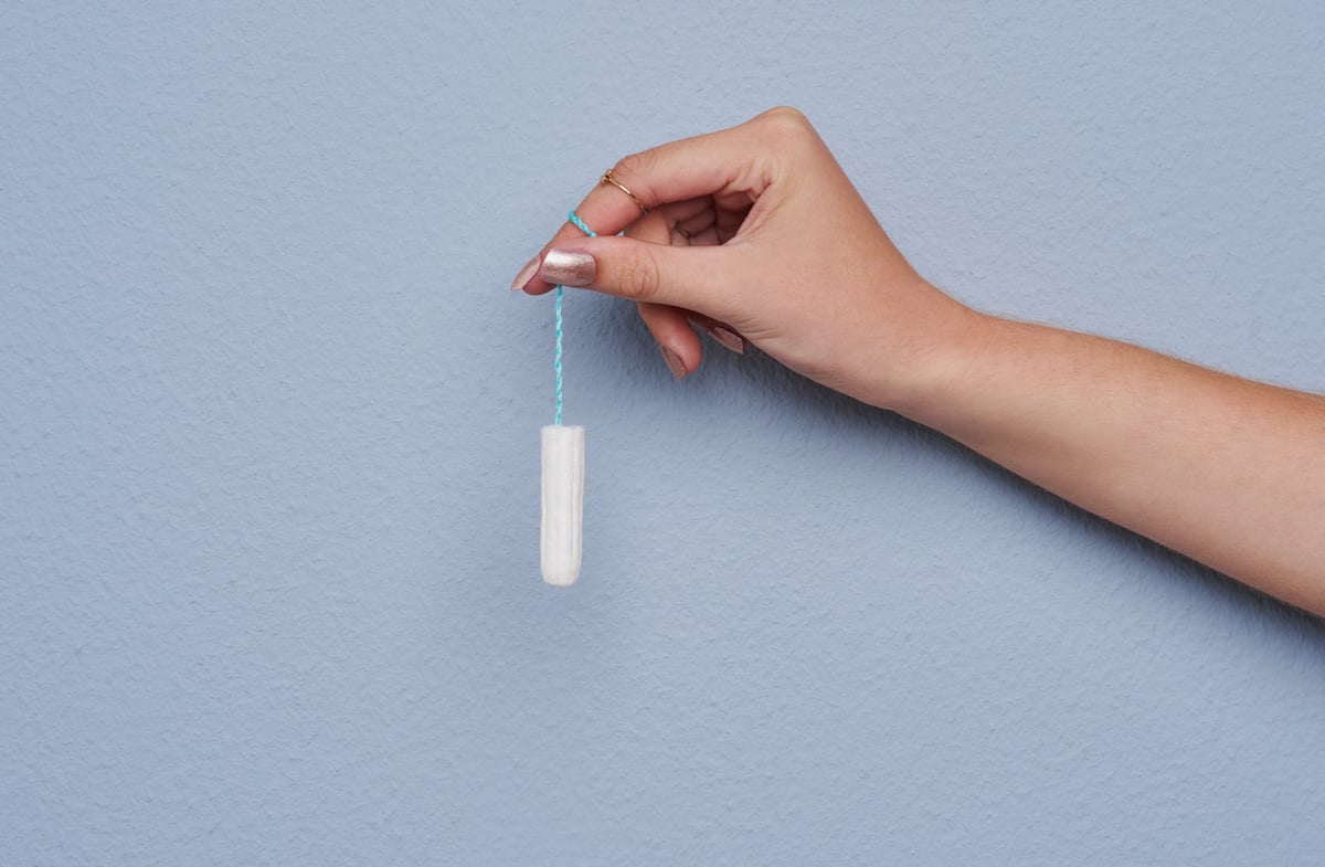 Cropped studio shot of a woman's hand holding a tampon against gray background