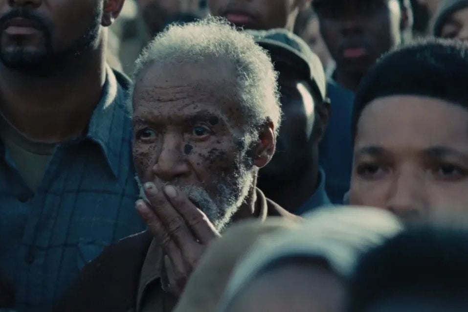 Still from Hunger Games Catching Fire;  A crowd scene of Black adults, with an older man pressing his fingers to his mouth.