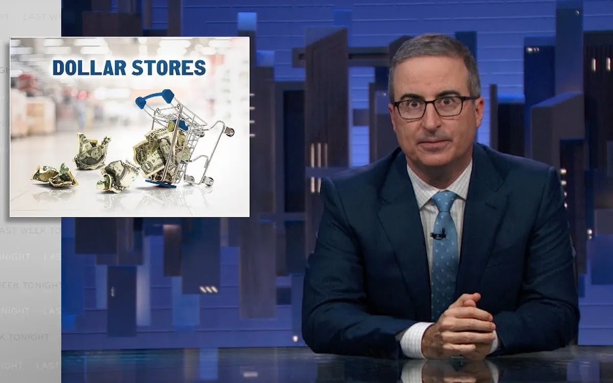 John Oliver sits at his news desk with a graphic on screen reading "dollar stores"