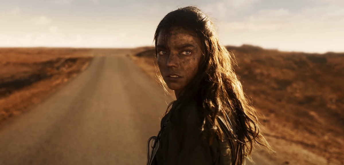 Furiosa (Anya Taylor-Joy) looks over her shoulder at the camera with a desert highway in front of her.