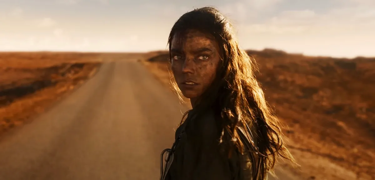 Furiosa (Anya Taylor-Joy) looks over her shoulder at the camera with a desert highway in front of her.