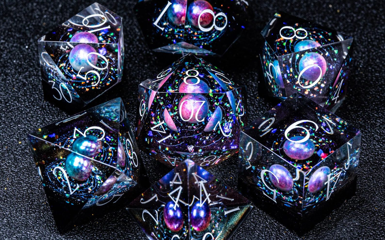 Clear resin dice with galaxies set inside, in jewel tones on black