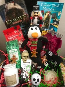A box full of items including a stuffed penguin in a Christmas scarf, little skull, creepy nutcracker, and a Krampus film.
