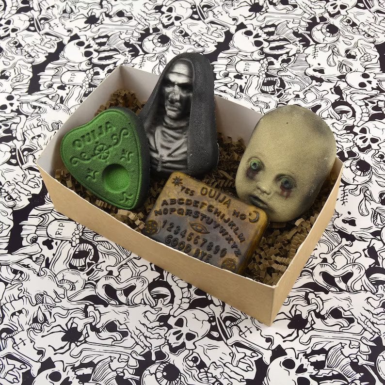 A box of four bath bombs shaped like a baby doll head, a planchette, a ouija board, and a ghostly nun.