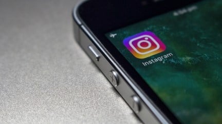 A stock photo of a phone on a flat surface, with the Instagram app icon in view on the top left of the phone screen.