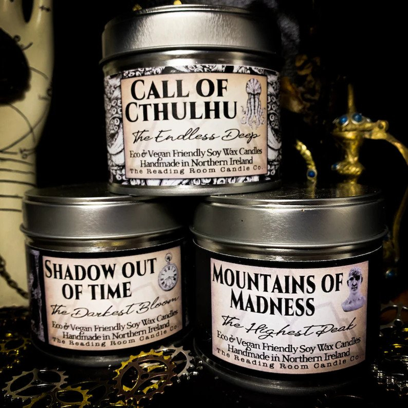 Three candle jars, black glass with silver tops. Each one has an apothecary style label with "Call of Cthullu", "The Mountains of Madness", and "Shadow Out of Time" written on them.