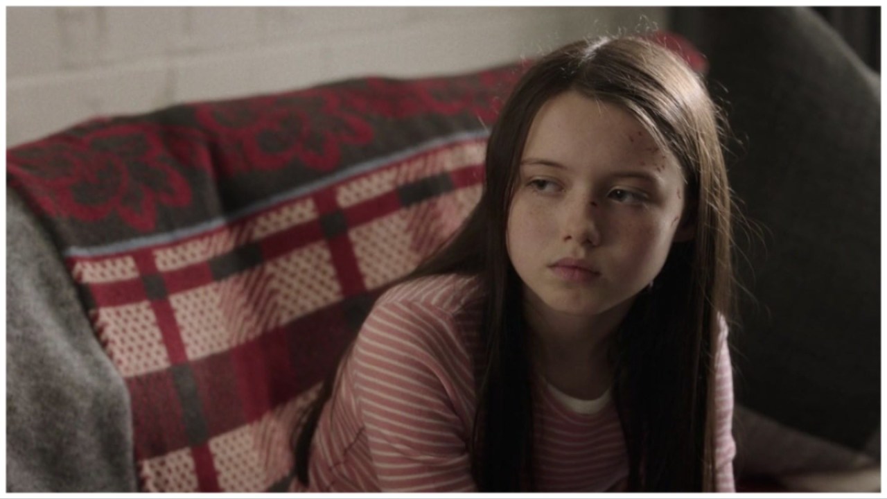 Cady (Violet McGraw) sits on a couch looking sad in 'M3gan'.
