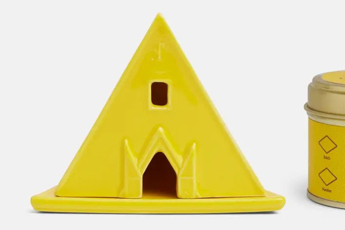 A yellow pyramidal incense burner/temple with a square window opening above a pentagonal door opening.