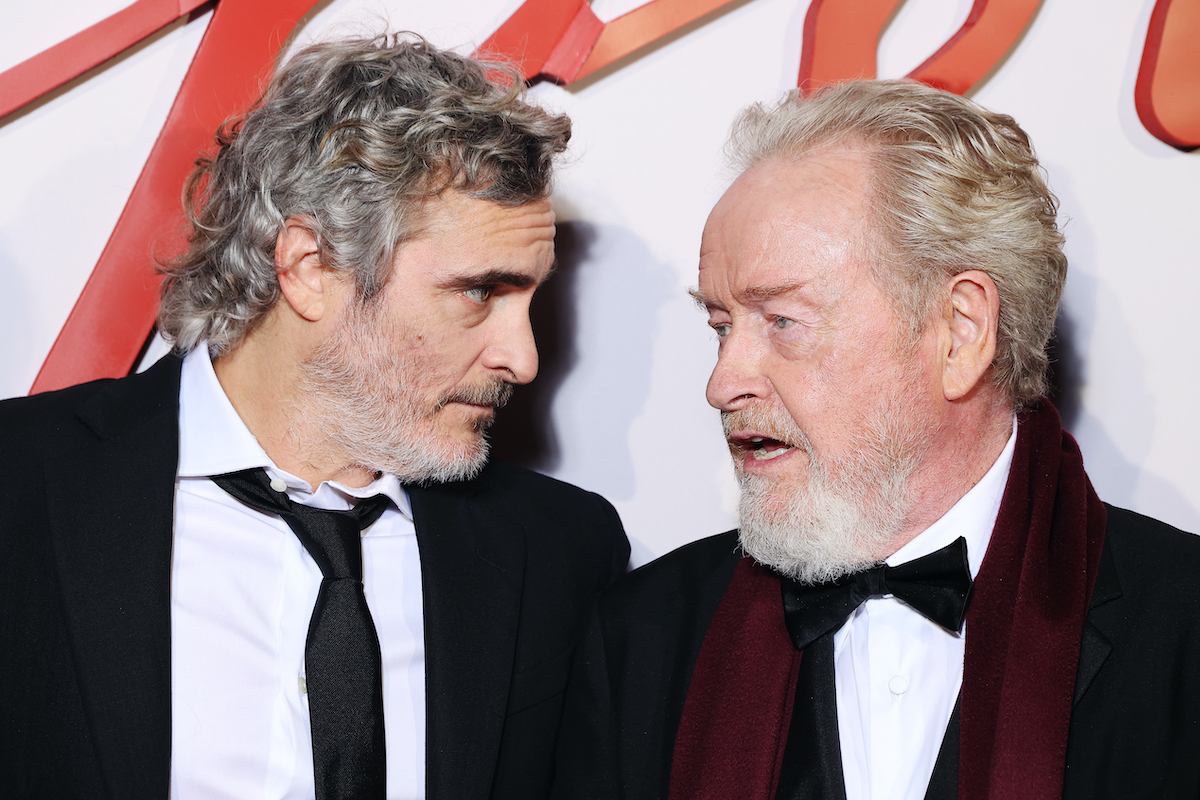 Joaquin Phoenix and Ridley Scott on the Napoleon red carpet, leaning into each other and talking close.