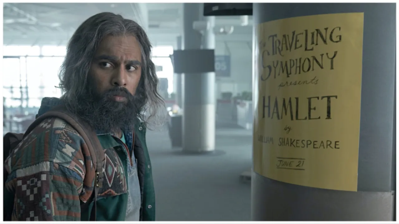 Jeevan Chaudhary (Himesh Patel) with a long beard, stares at a poster for the Traveling Symphony in 'Station Eleven'.