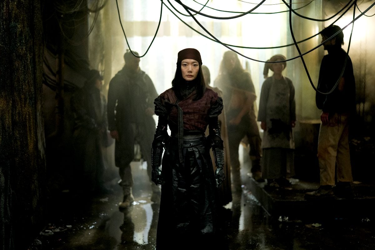 Bae Doona as Nemesis stands in an industrialized room in 'Rebel Moon Part One A Child of Fire.'