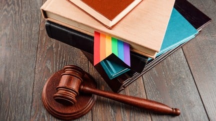 A stack of books with an LGBTQ+ bookmark next to a judge's gavel