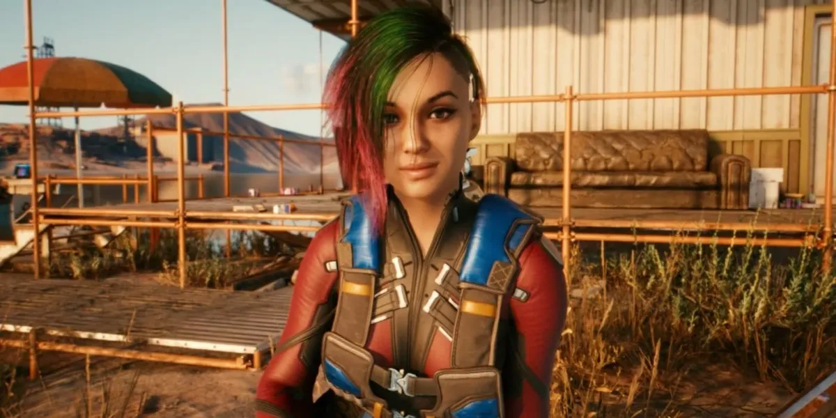 A girl with pink and green hair smiles into the camera in "Cyberpunk 2077"