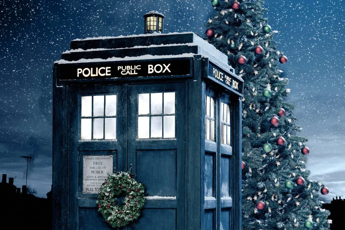 Doctor Who's TARDIS with a Christmas wreath on the door, in front of a Christmas tree