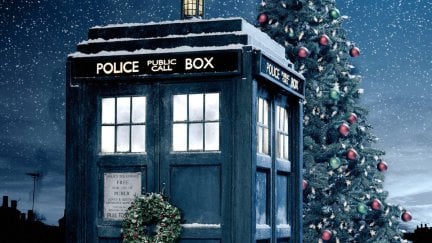 Doctor Who's TARDIS with a Christmas wreath on the door, in front of a Christmas tree