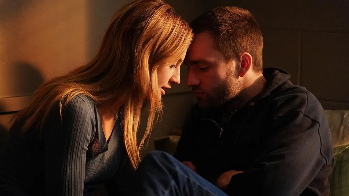 Image of Grace Van Patten and Jackson White in a scene from 'Tell Me Lies.' Van Patten is a young white woman with long strawberry blonde hair. White is a young white man with closely cropped brown hair and a thin beard. They are in casual clothes and sitting on the floor leaning into each other romantically. 