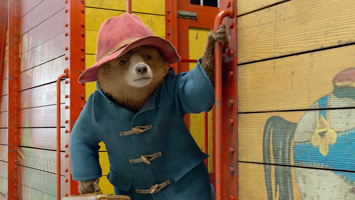 Paddington the Bear in blue jacket and red hat rides on train