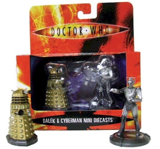An orange and black patterned display box with the Doctor Who logo at the top and a gold dalek and silver cyberman inside. In front of it a gold dalek, a mostly gold coloured round topped conical creature with two lights on top of its head like eyes and a plunger and a whisk shape device where arms would be, and a silver cyberman, an inhuman looking robot.