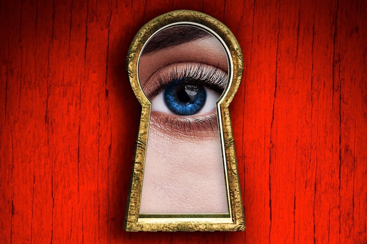 A woman'e eye peers through a keyhole against a red background