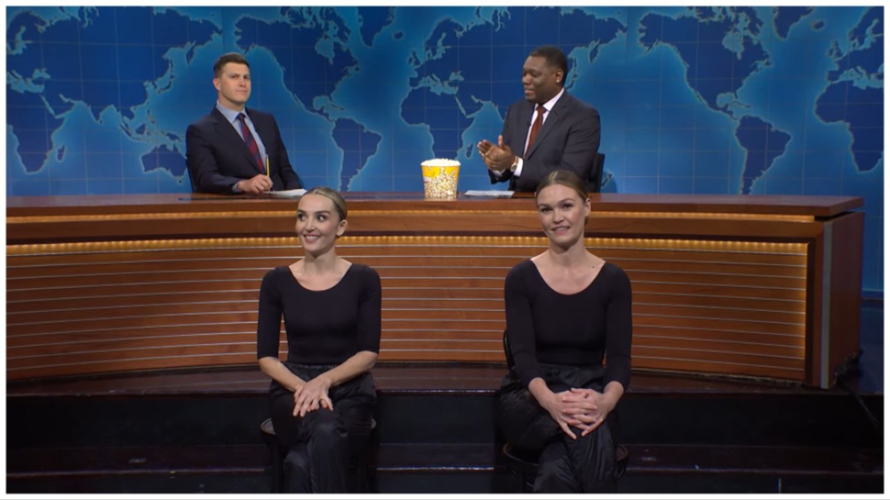 Chloe Fineman and Julia Stiles sit on chairs in black leotard while Colin Jost and Michael Che sit behind them at the Weekend Update desk on 'Saturday Night Live.'