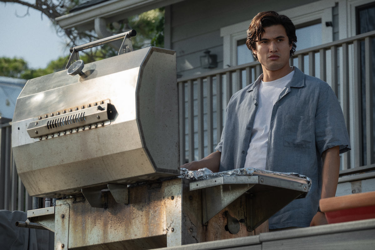 In a scene from May December, Charles Melton stands over a barbeque grill.