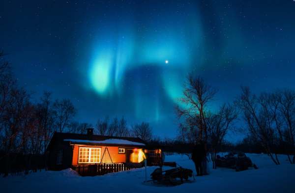 A cabin in the snow at night, with the Northern Lights in the background.