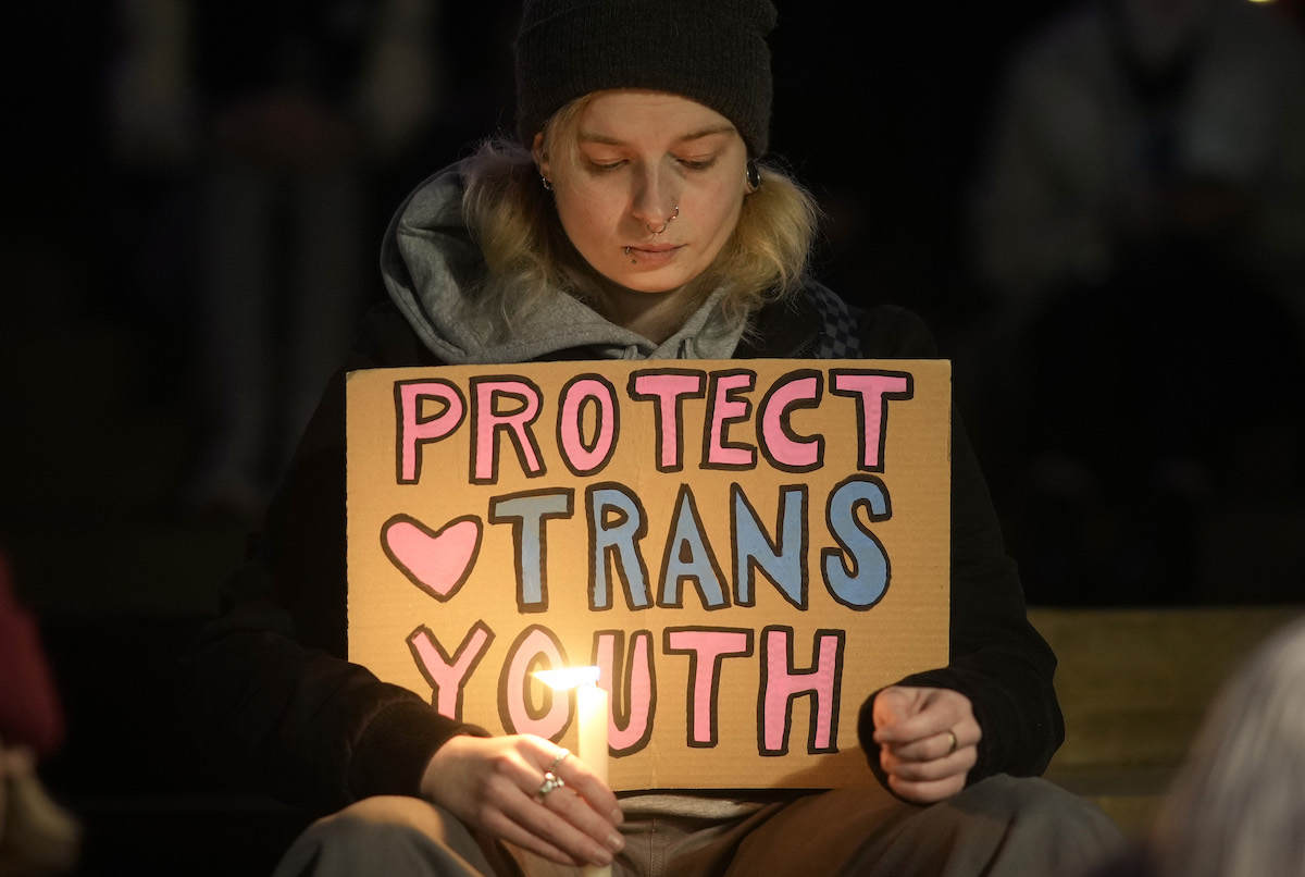 A person at a Brianna Ghey vigil holding a sign that reads, "Protect trans youth."
