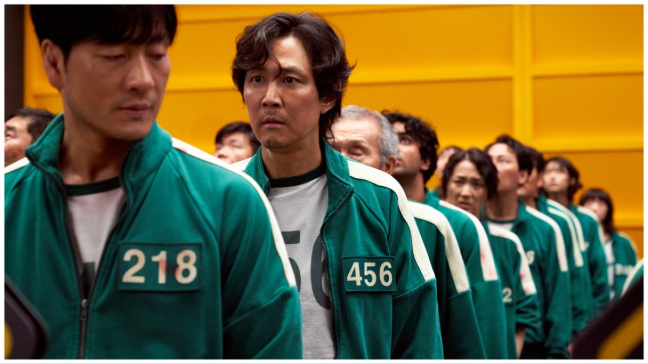 Park Hae-soo and Lee Jung-jae stand in a line where everyone is wearing numbered green tracksuits in 'Squid Game'.
