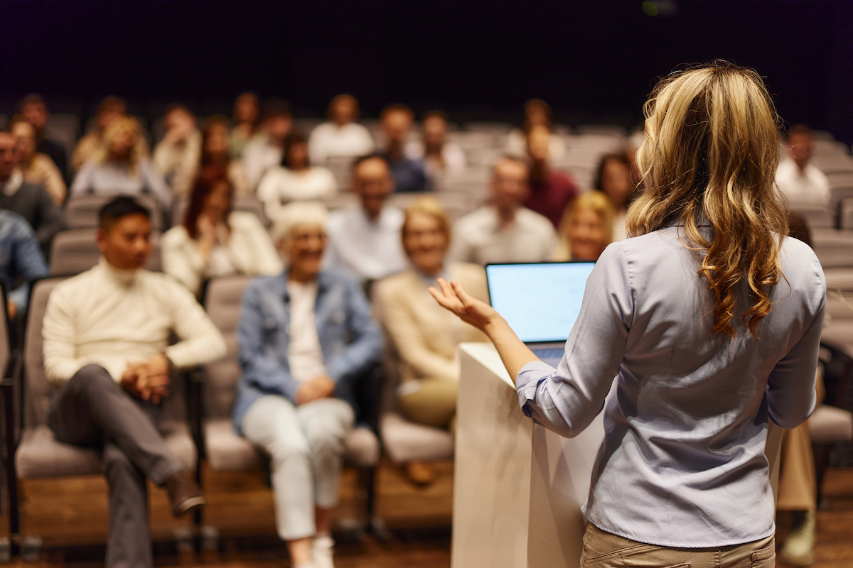 Rear view of a female public speaker talking to an audience at a conference