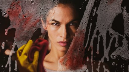 A woman cleans blood off of a window with a rag in 