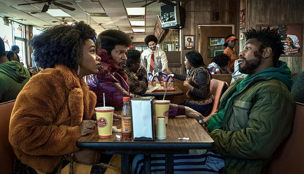	 John Boyega, Teyonah Parris, and Jamie Foxx sit at a diner table in They Cloned Tyrone