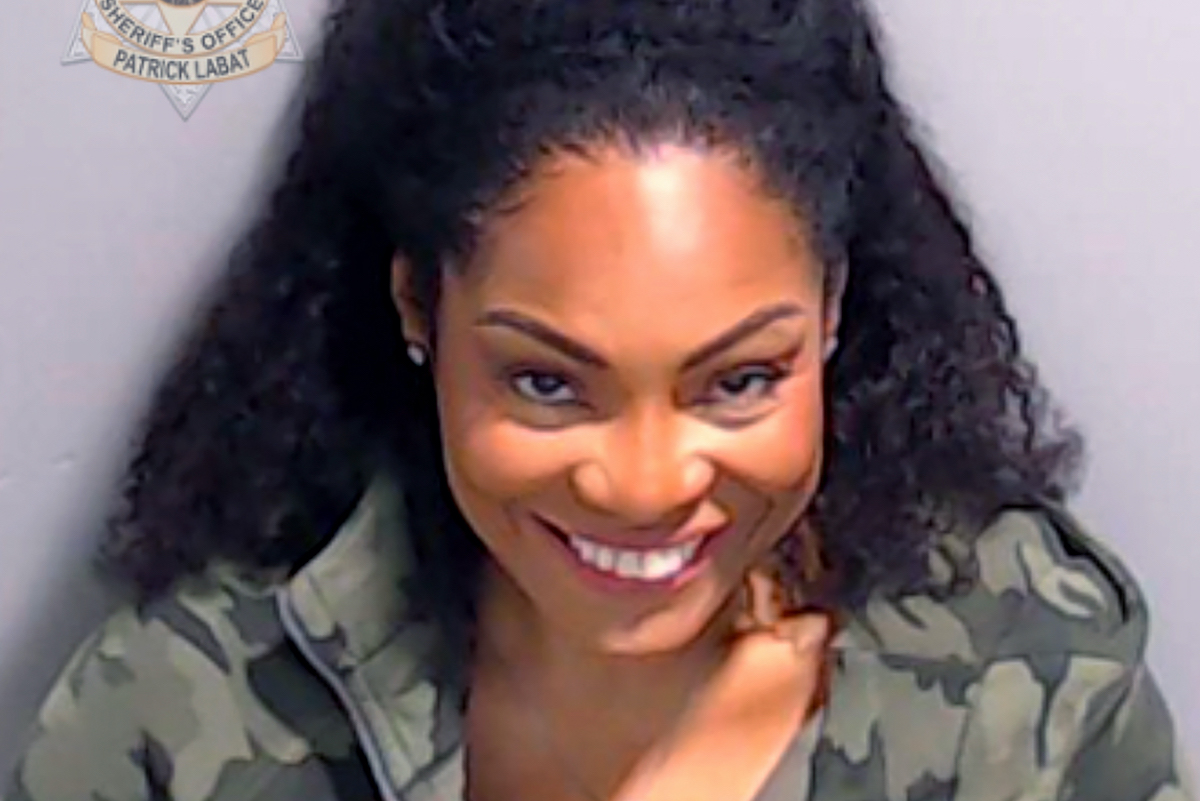 A Black woman (Kutti) gives a Joker-esque smile in a police mugshot
