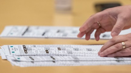 Hands sorting piles of election ballots on a table.