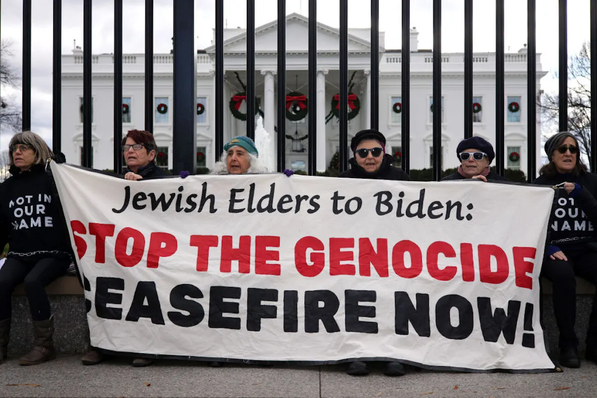 18 elderly Jewish women hold up a banner in front of the White House reading, "Jewish Elders to Biden: Stop the Genocide, Ceasefire Now."