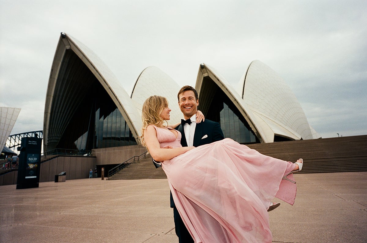 Glen Powell carrying Sydney Sweeney in front of the Sydney opera house