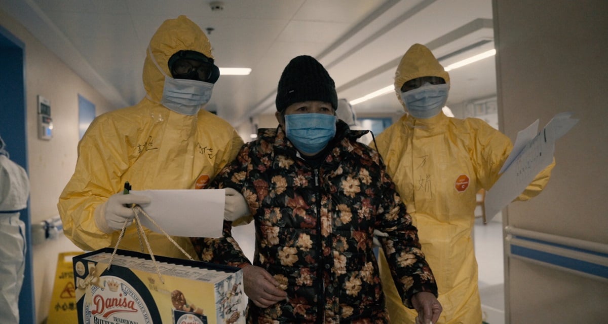 two nurses in Haz-mat gear escort a masked patient from hospital during COVID 19 pandemic