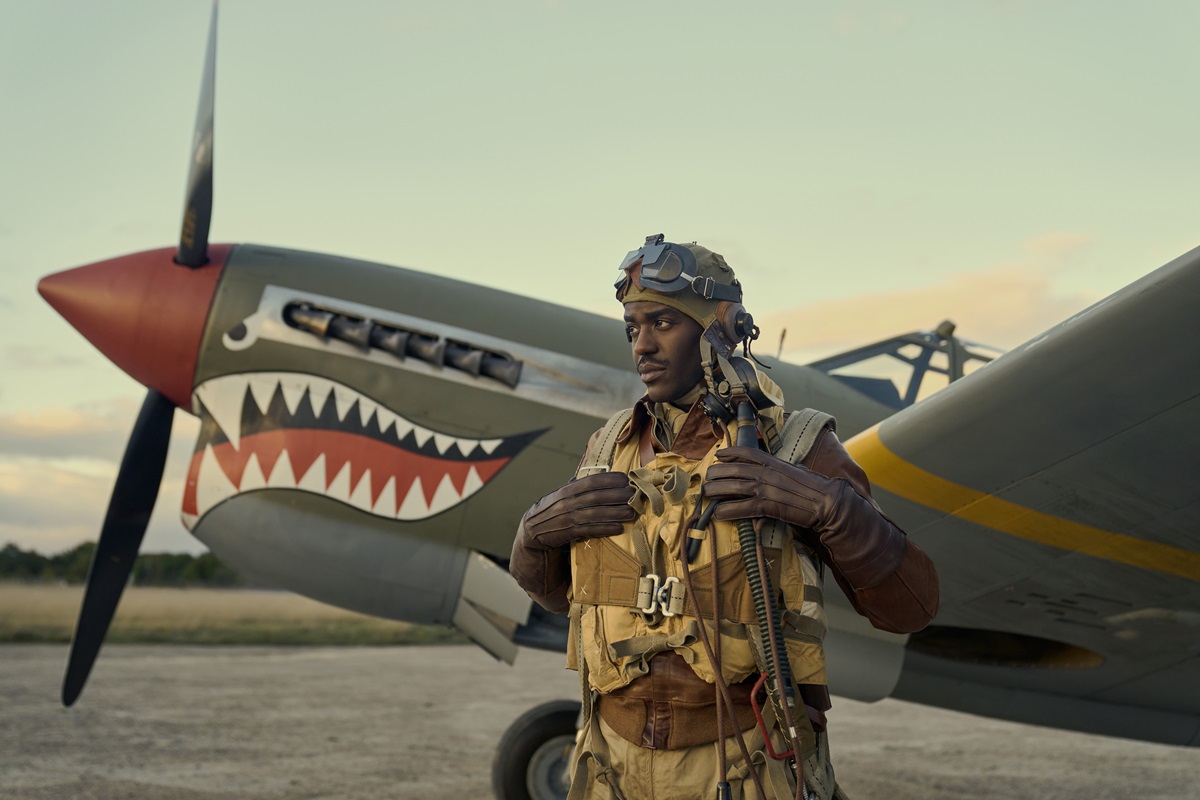 Ncuta Gatwa wearing fighter pilot uniform standing in front of a plane in 'Masters Of The Air'