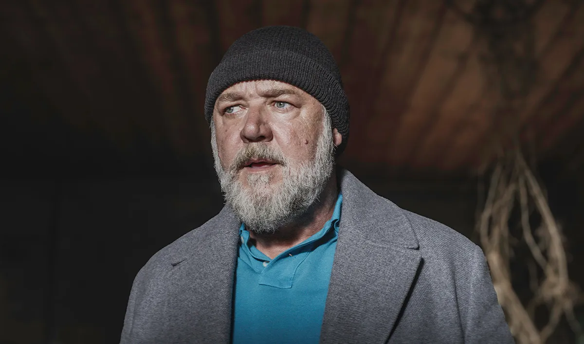 Russell Crowe standing with a beanie on looking shocked