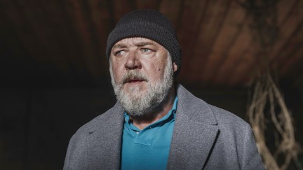 Russell Crowe standing with a beanie on looking shocked