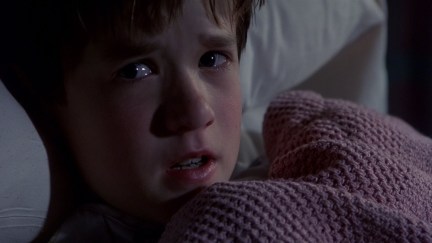 little boy hiding under the covers in bed looking terrified