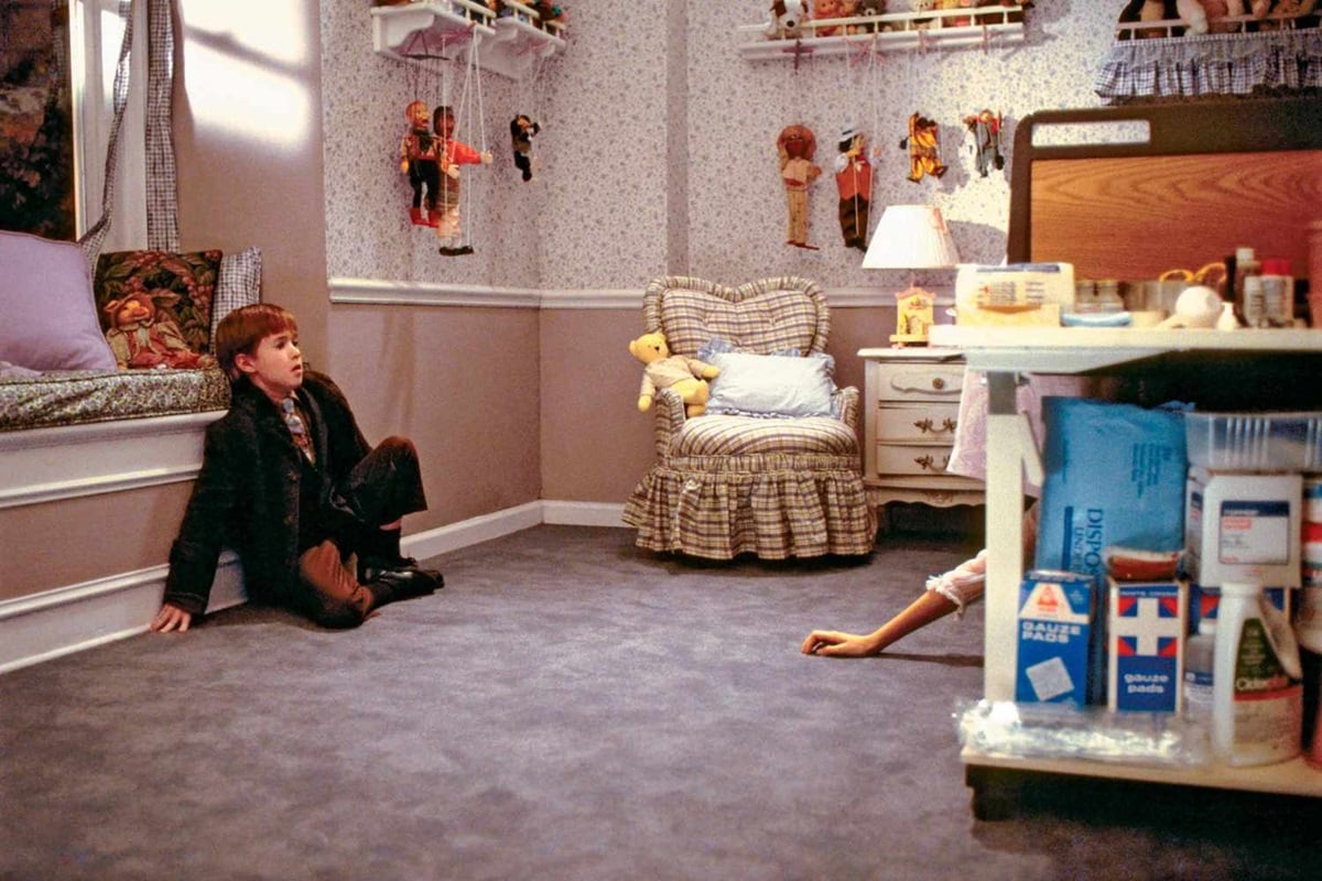 a young boy cowers on the floor of a girly bedroom while a girl's arm reaches for him from under the bed