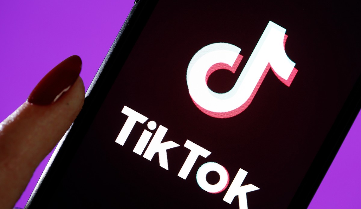 A hand holds a phone with TikTok opened on it