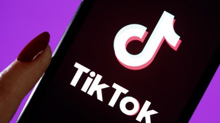 A hand holds a phone with TikTok opened on it