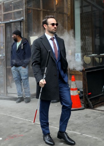 Matt Murdock walks down the street, wearing sunglasses and holding his cane.
