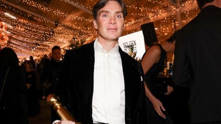 Cillian Murphy holds his Golden Globe statue looking uncomfortable in a crowd.