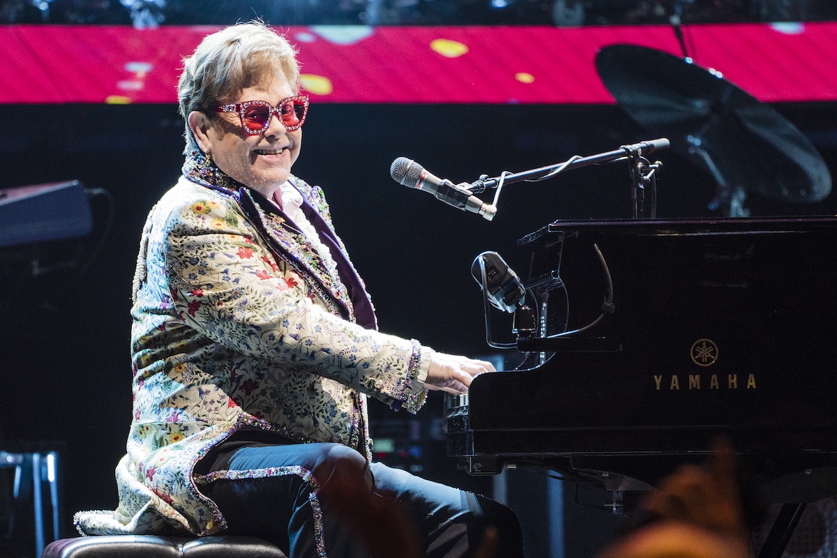 Elton John at a piano in bright pink glasses