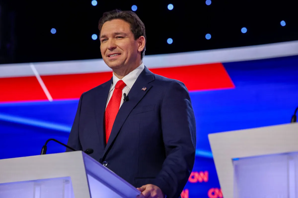 Ron DeSantis gives an awkward smile from a podium.