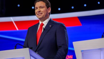 Ron DeSantis gives an awkward smile from a podium.