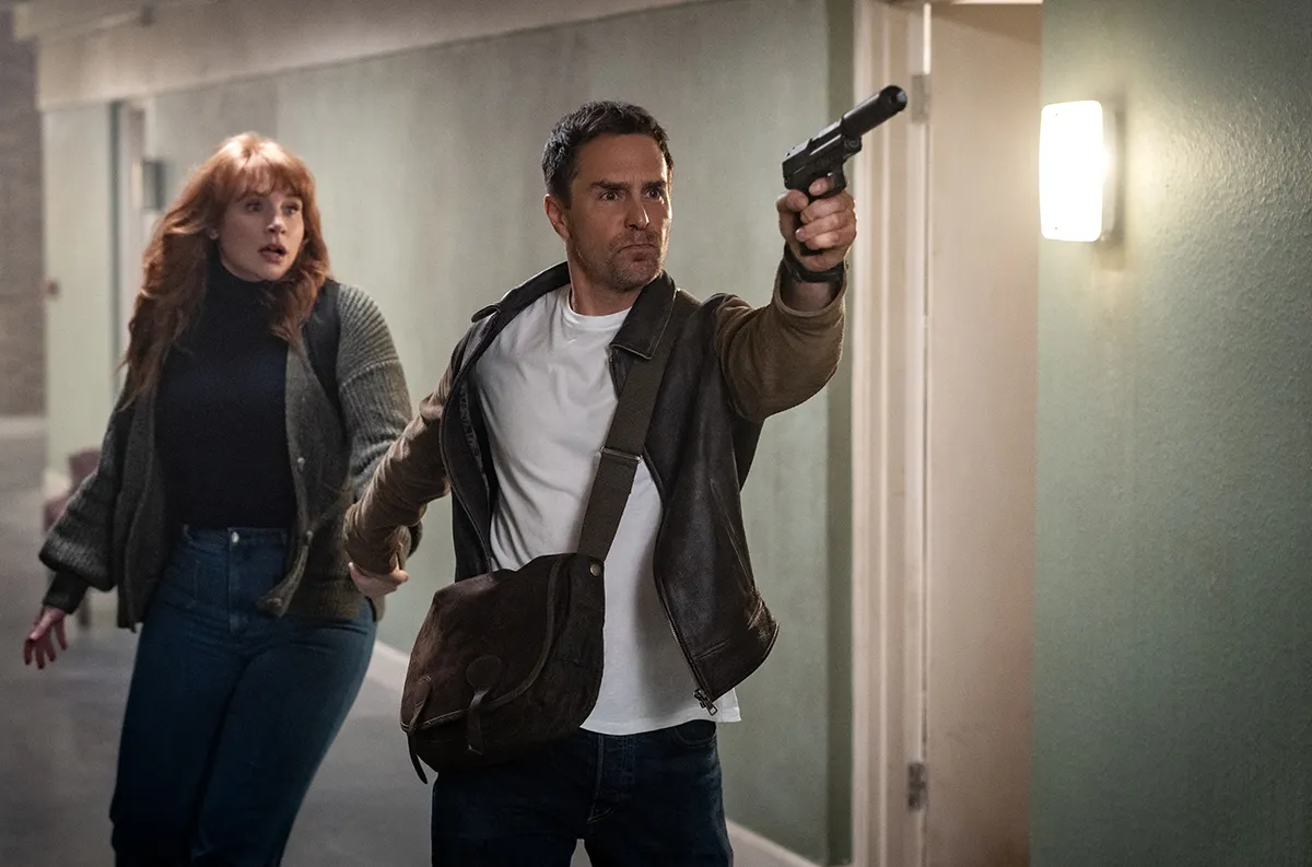 Sam Rockwell with a gun walking down the hallway with Bryce Dallas Howard