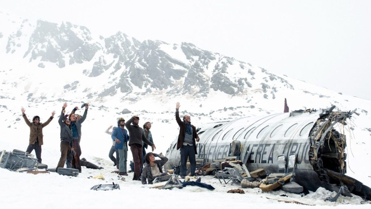 Men stand in the snow beside a wrecked airplane in 'Society of the Snow'.